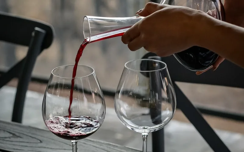 person pouring wine from decanter on wineglass - tempranillo vs pinot noir